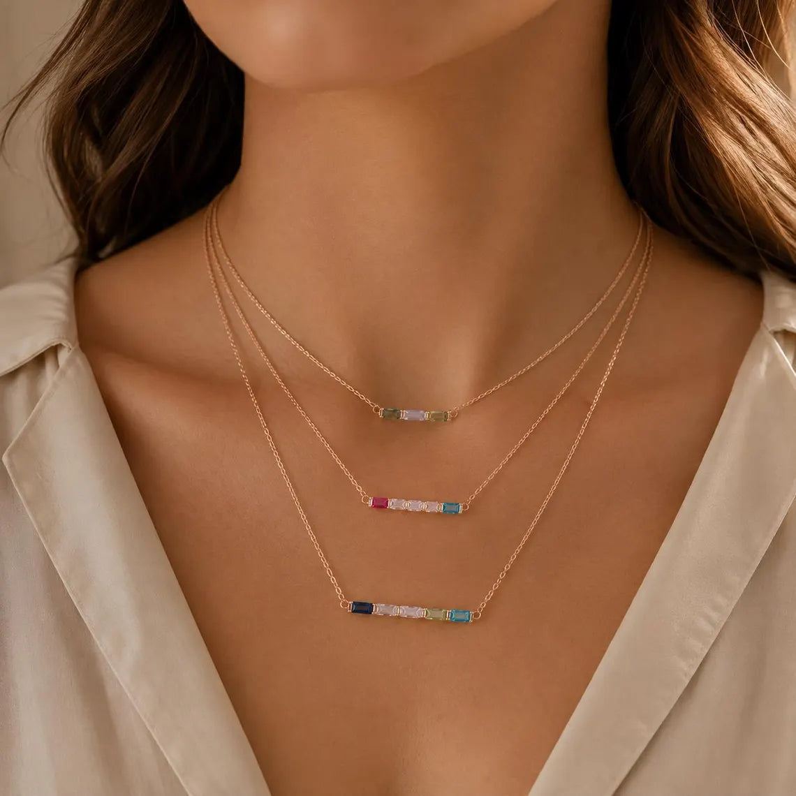 Three layered baguette birthstone necklaces worn together on a model's neckline