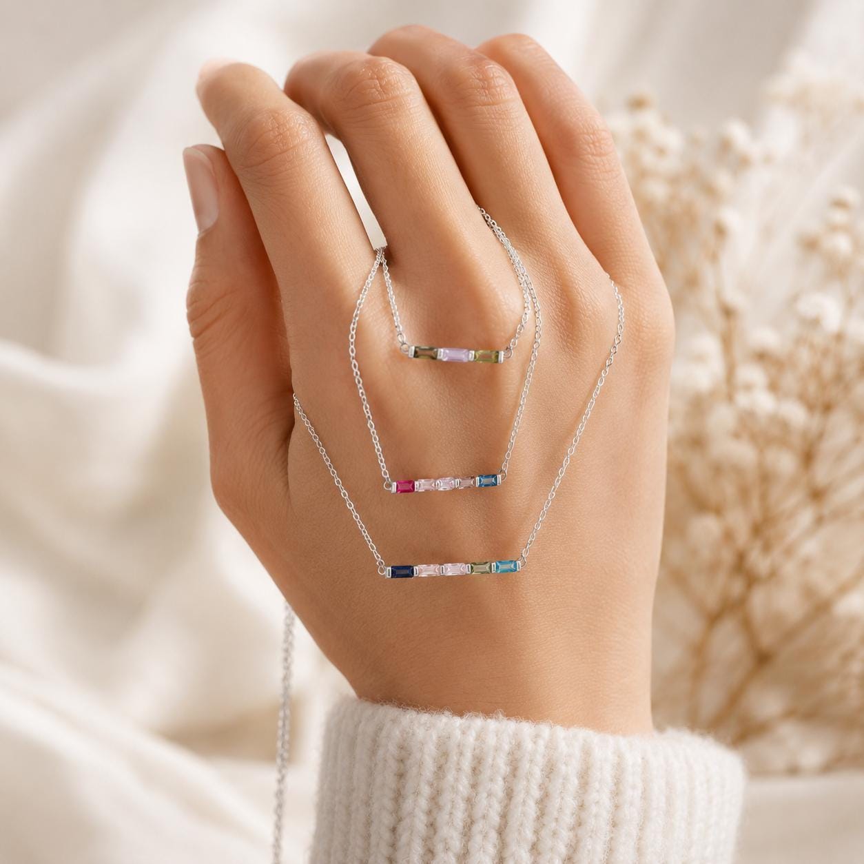 Silver baguette birthstone necklace with four birthstones held over a woman's hand