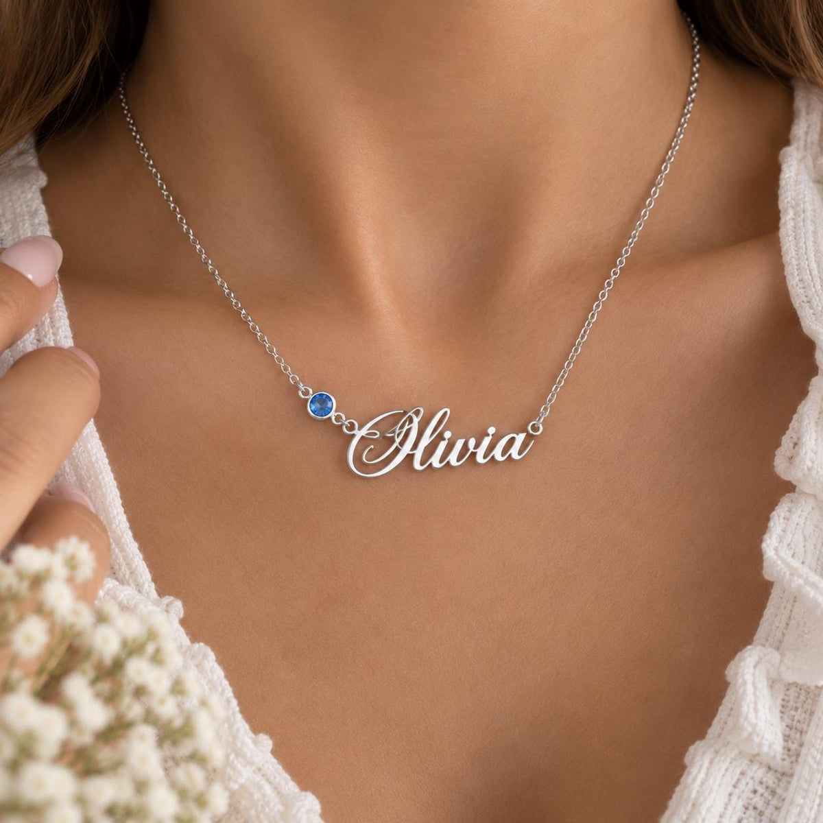Silver tone name necklace with a blue stone worn on the neck