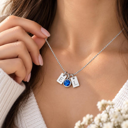 Silver tone initial tag necklace with a blue birthstone charm worn on the neck