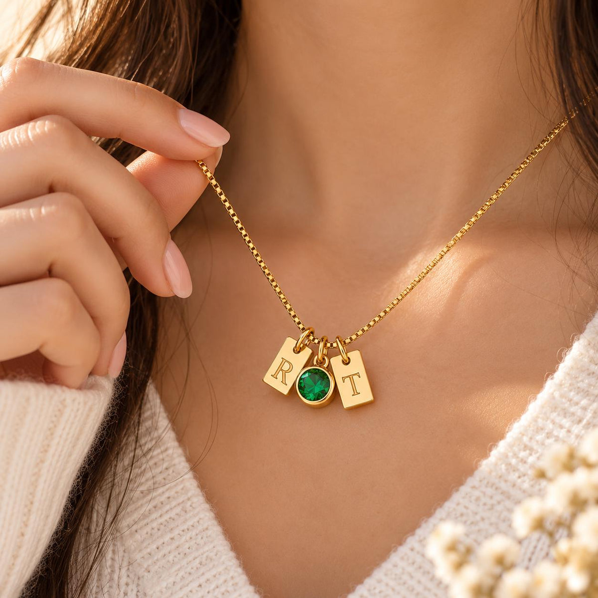 Gold tone initial tag necklace with a green stone worn on the neck