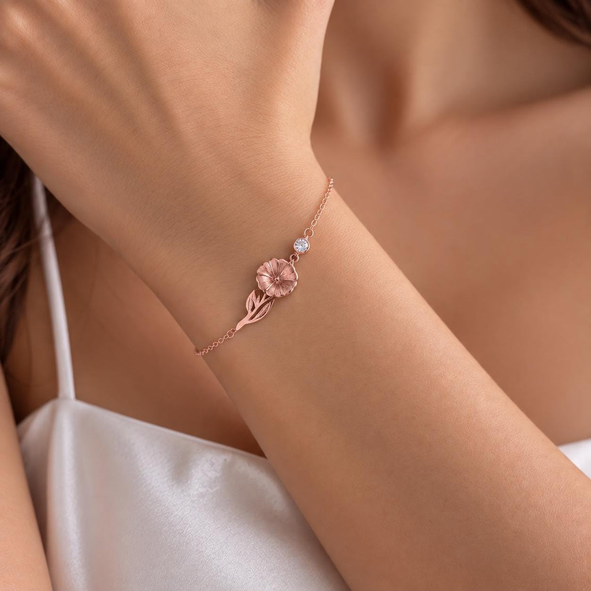 Rose gold tone birth flower bracelet with a pink stone worn on the wrist