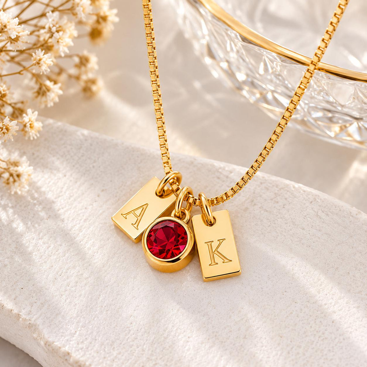 Gold tone initial tag necklace with a red stone