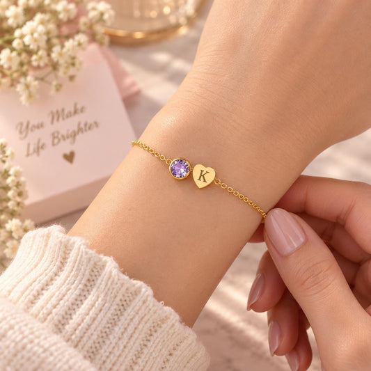 Gold tone initial bracelet with a pink stone worn on the wrist