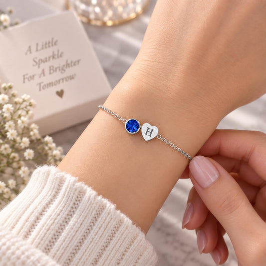 Heart initial birthstone bracelet with a blue stone and letter charm worn on the wrist