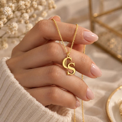 Gold tone double initial charm held between the fingers