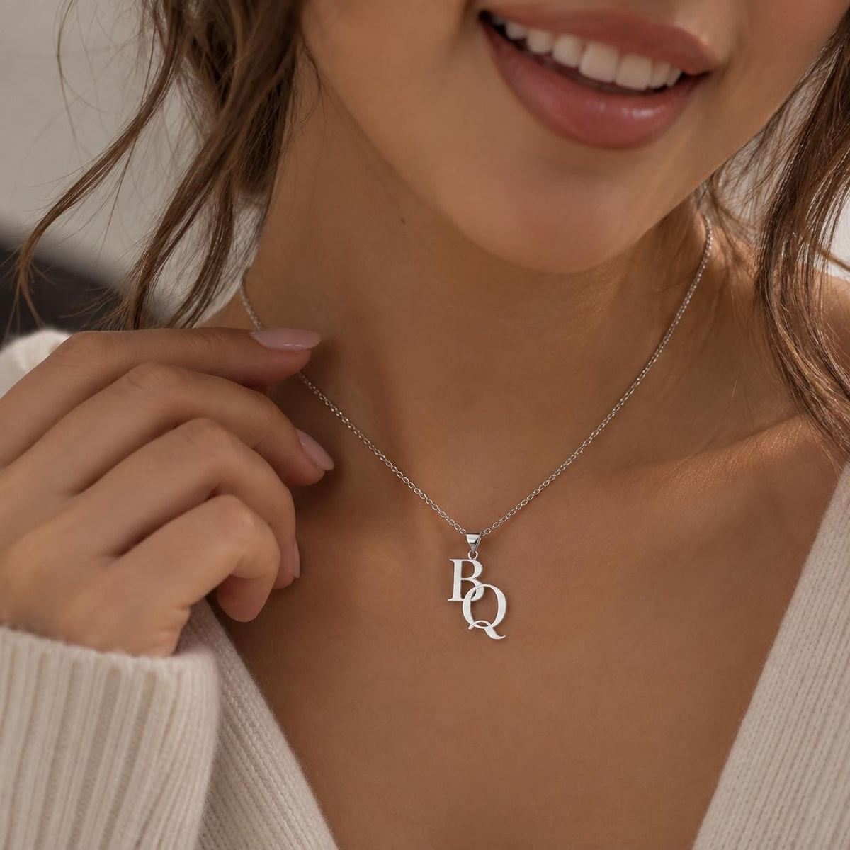 Silver tone double initial necklace worn on the neck, close up